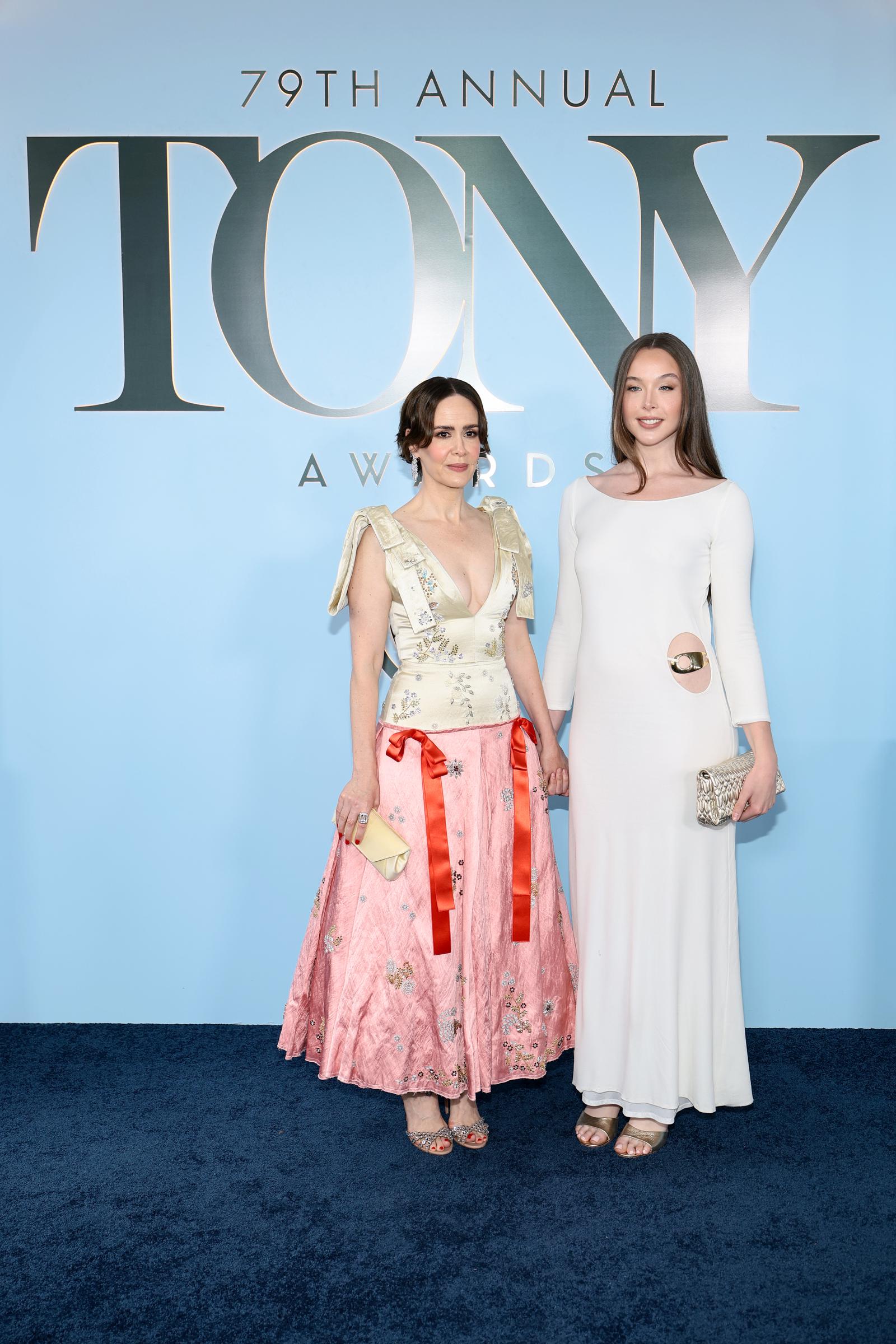 Sarah Paulson and Ella Beatty turn heads and hold hands as they arrive at the 79th Annual Tony Awards. Sarah sports an embroidered top with a bow-accented pink skirt, while Ella coordinates beautifully in a long-sleeved white column gown.