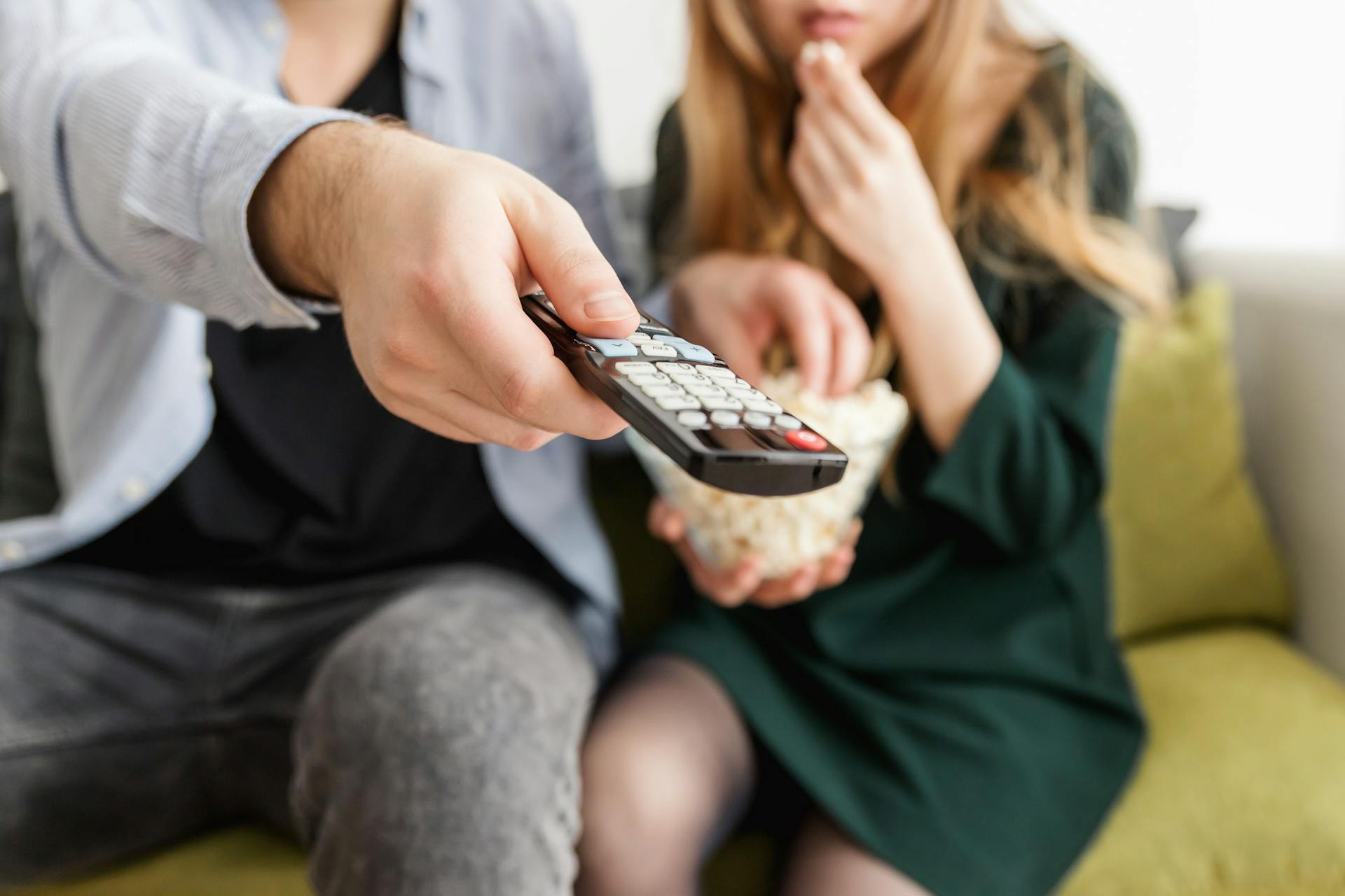 Mężczyzna trzymający pilota podczas jedzenia popcornu z żoną | Źródło: Pexels