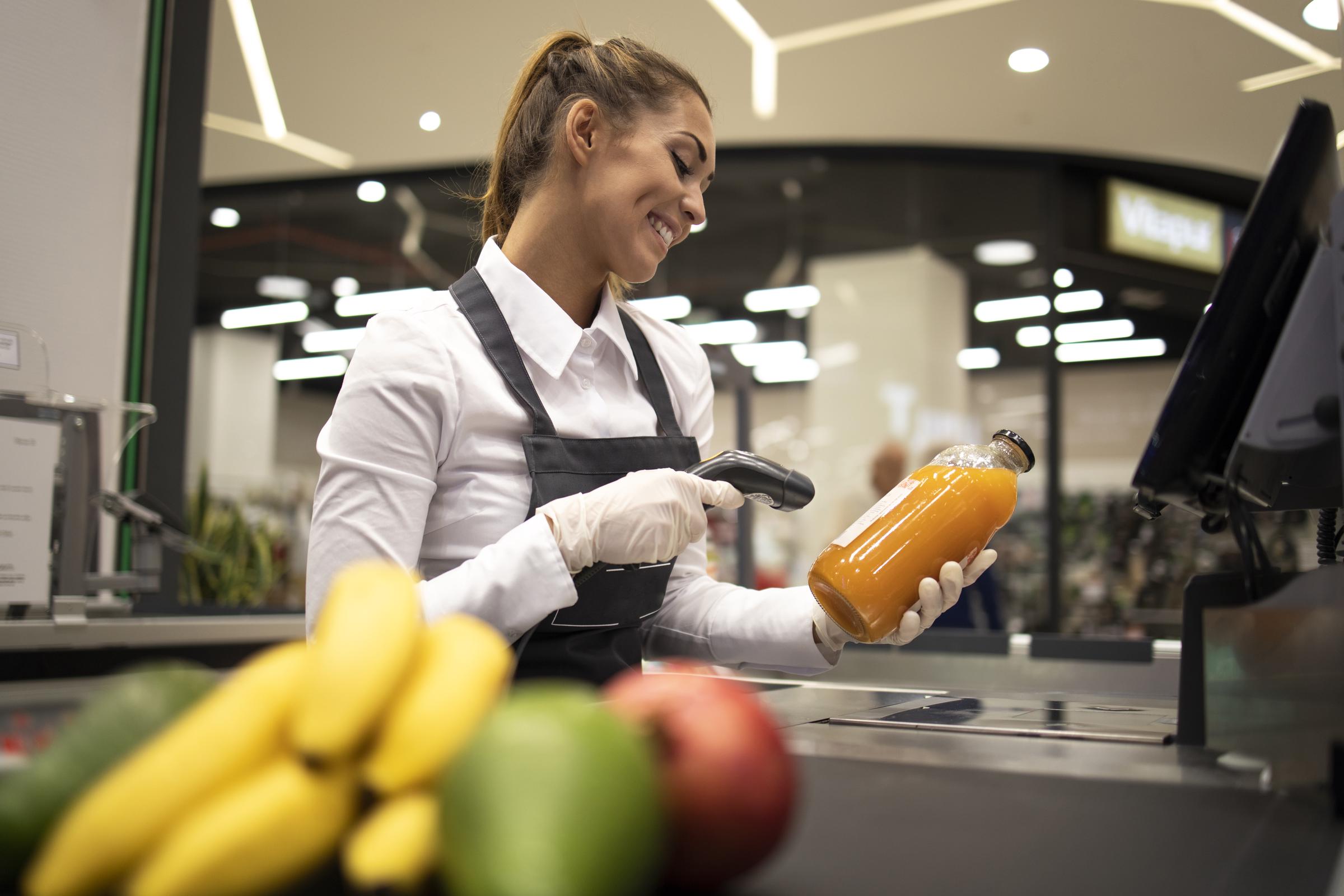 Portrait of female cashier in supermarket scanning bar code of products for sale | Source: Magnific